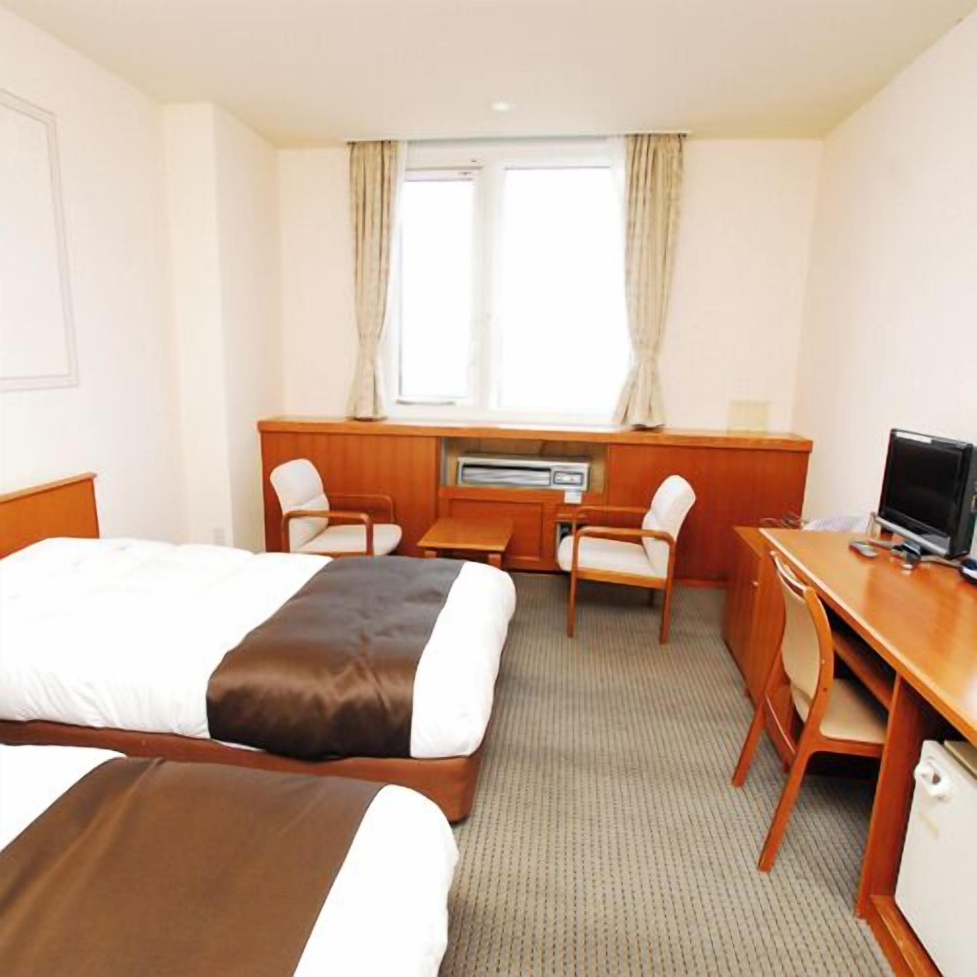 A hotel room with two beds, a desk, a chair, a television, and a window with curtains.