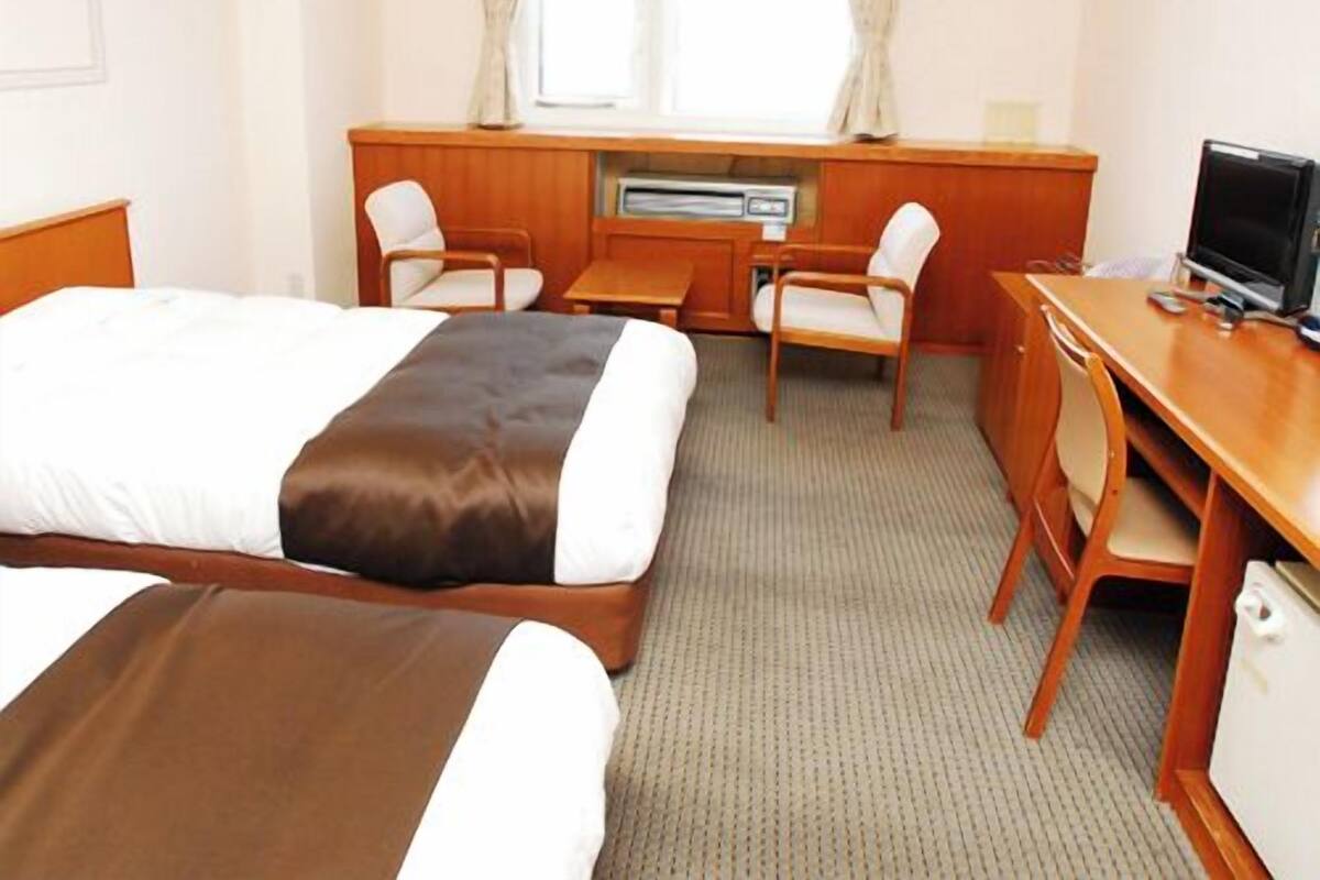 A hotel room with two beds, a desk, a chair, a television, and a window with curtains.