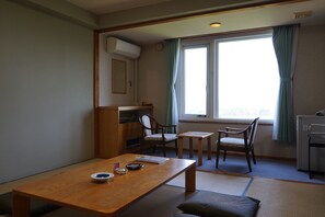 Ett rum med ett träbord, två stolar, ett litet skrivbord och ett fönster med gardiner.