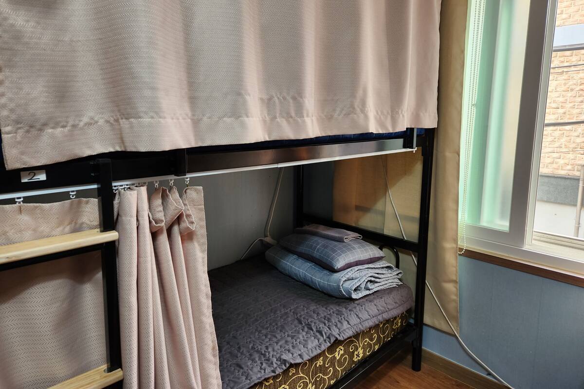 A bunk bed with a patterned curtain and a window with a view of a brick building.