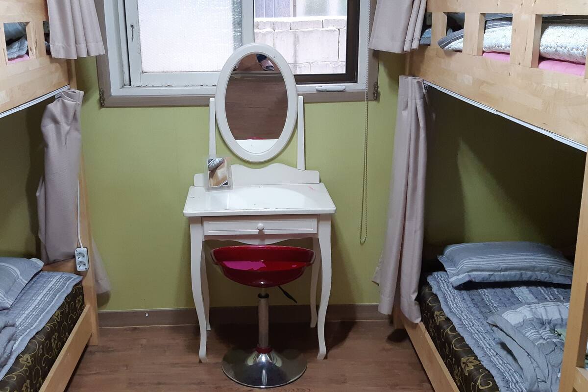 A dormitory room with bunk beds, a small desk with a mirror, and a red chair.