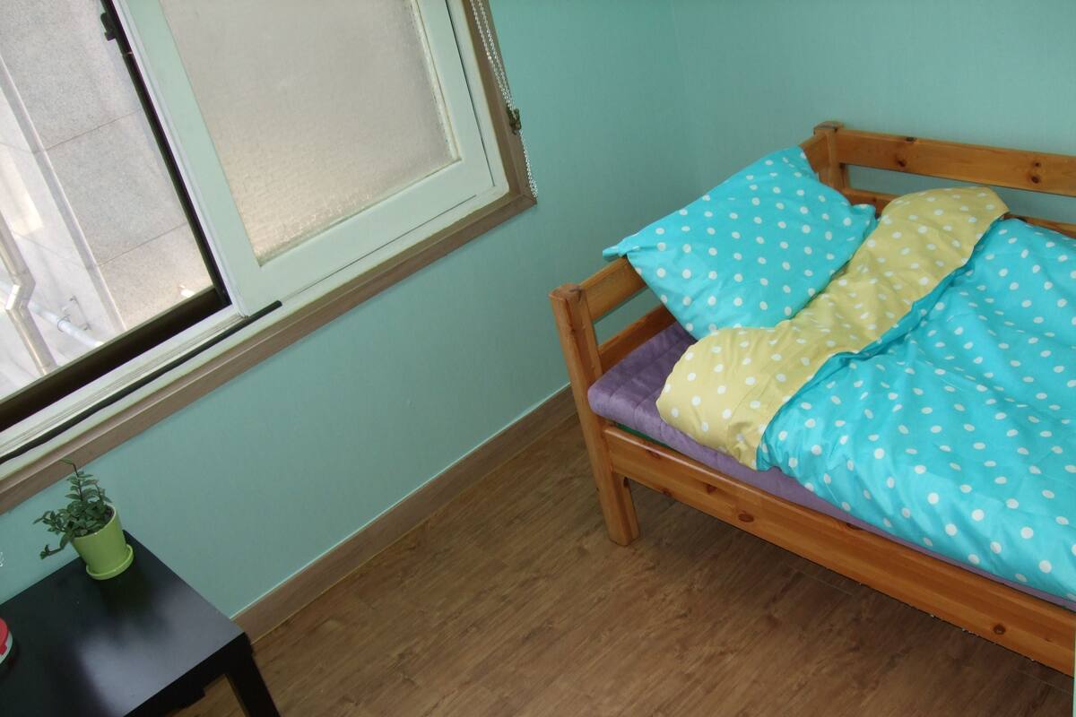 A small room with a wooden bed, a window, and a small table with a plant.