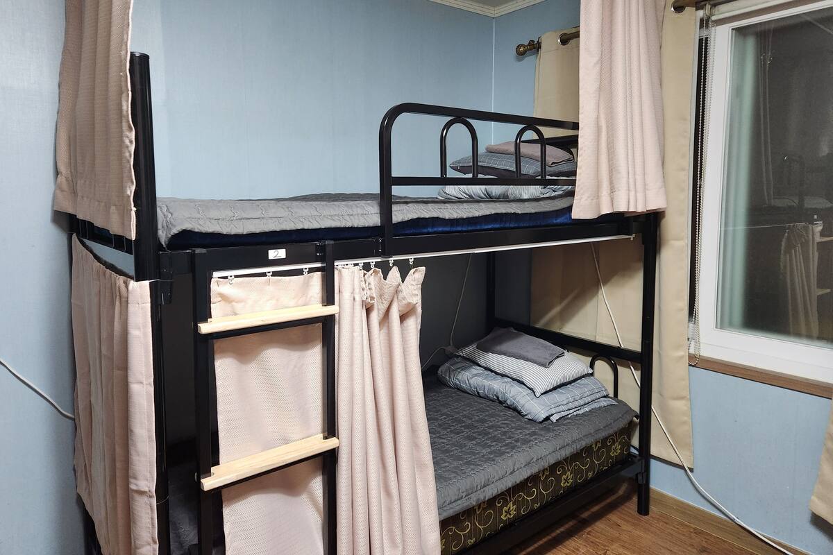 A bunk bed room with a window, curtains, and a bed with pillows.