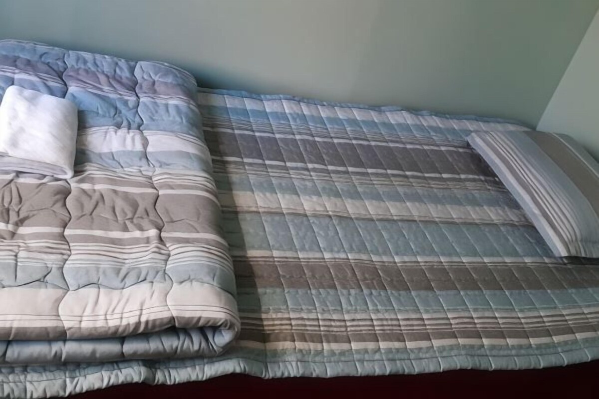 A bed with a striped quilt and a folded blanket.