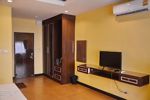 A hotel room with a wooden wardrobe, a flat-screen TV, and an air conditioning unit on the wall.