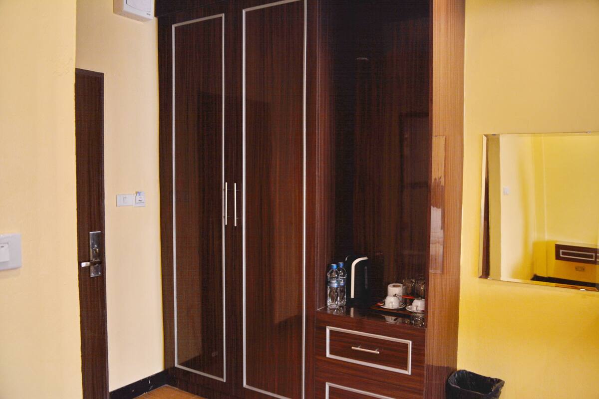 A room with a wooden wardrobe, a small shelf with toiletries, and a mirror on the wall.