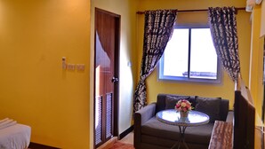 A room with yellow walls, a brown sofa, a small round table with a vase of flowers, and a window with patterned curtains. - Taj Place Residency (Pattaya)