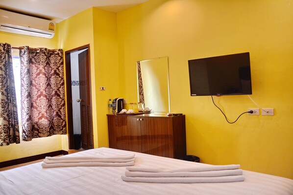 A hotel room with a bed, a wooden dresser, a flat-screen TV mounted on the wall, and a window with patterned curtains.