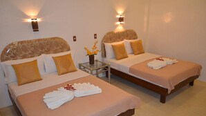 Habitación de hotel con dos camas, cada una con cabecero, una mesita con un florero y luces fijadas a la pared.