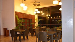 Un restaurante con varias mesas y sillas, ventanas amplias y lámparas colgantes.