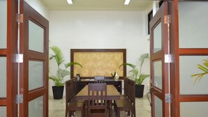 Un salón de conferencias con una mesa de madera y sillas, dos plantas en macetas y un panel decorativo en la pared.