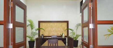 A conference room with a wooden table and chairs, two potted plants, and a decorative wall panel.