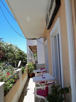 Un balcón exterior estrecho con una mesa y sillas blancas, una planta en maceta y una antena parabólica.
