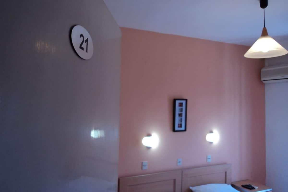 A hotel room with a number '21' on the wall, a bed with a headboard, bedside tables, and a hanging light fixture.