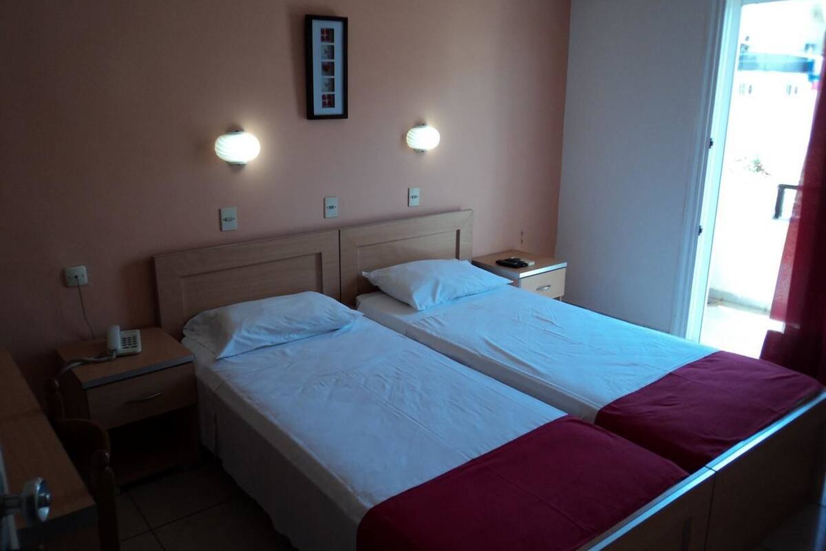A double bed with a red blanket, bedside tables, a phone, and wall-mounted lights.