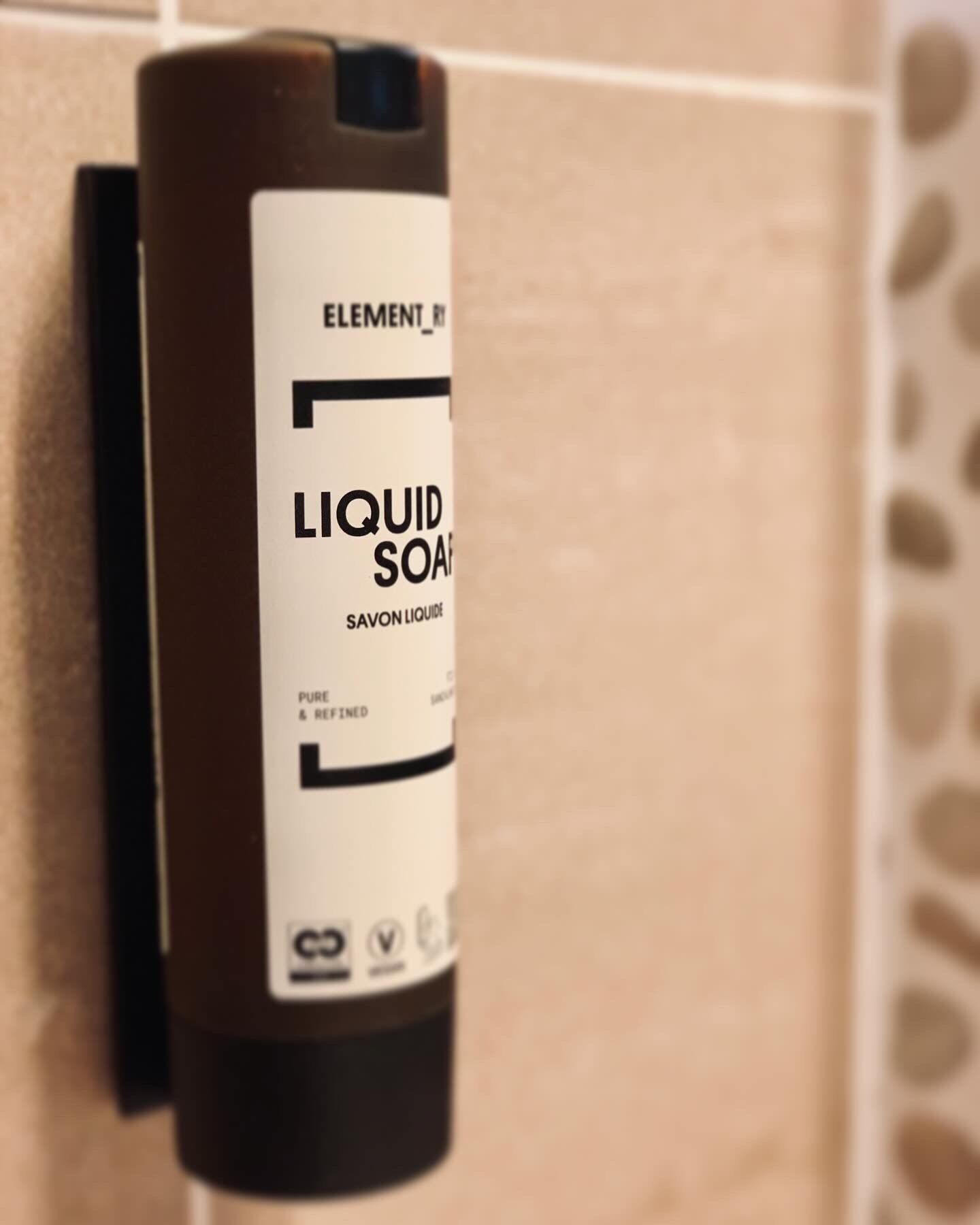 A bottle of Element liquid soap on a tiled wall.