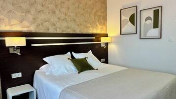 A neatly made bed with white linens and a green accent pillow, a small white bench, and two wall-mounted lamps.