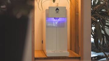 Een waterdispenser met een plant ernaast, een hangende lamp en een houten plank.