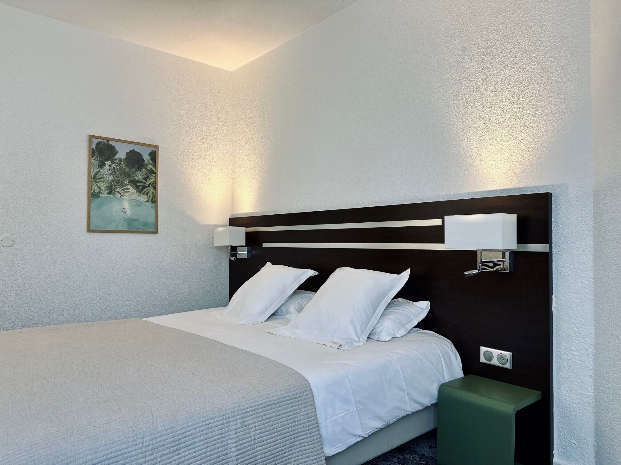 A neatly arranged hotel room with a bed, bedside table, and a wall-mounted light fixture.