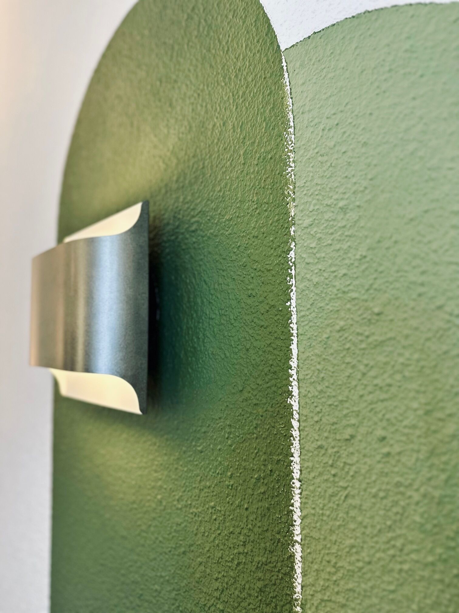 A close-up of a textured green wall with a metallic object, possibly a handle or fixture, attached to it.