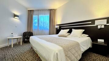Habitación de hotel con una cama grande, una mesita, una silla y una ventana con cortinas.