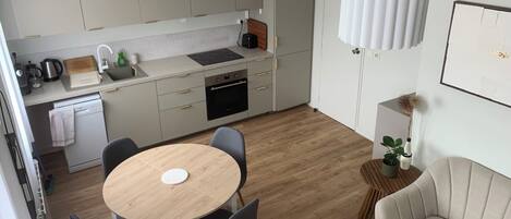 A modern kitchen with a round dining table, grey chairs, a beige sofa, and a small side table with a plant.