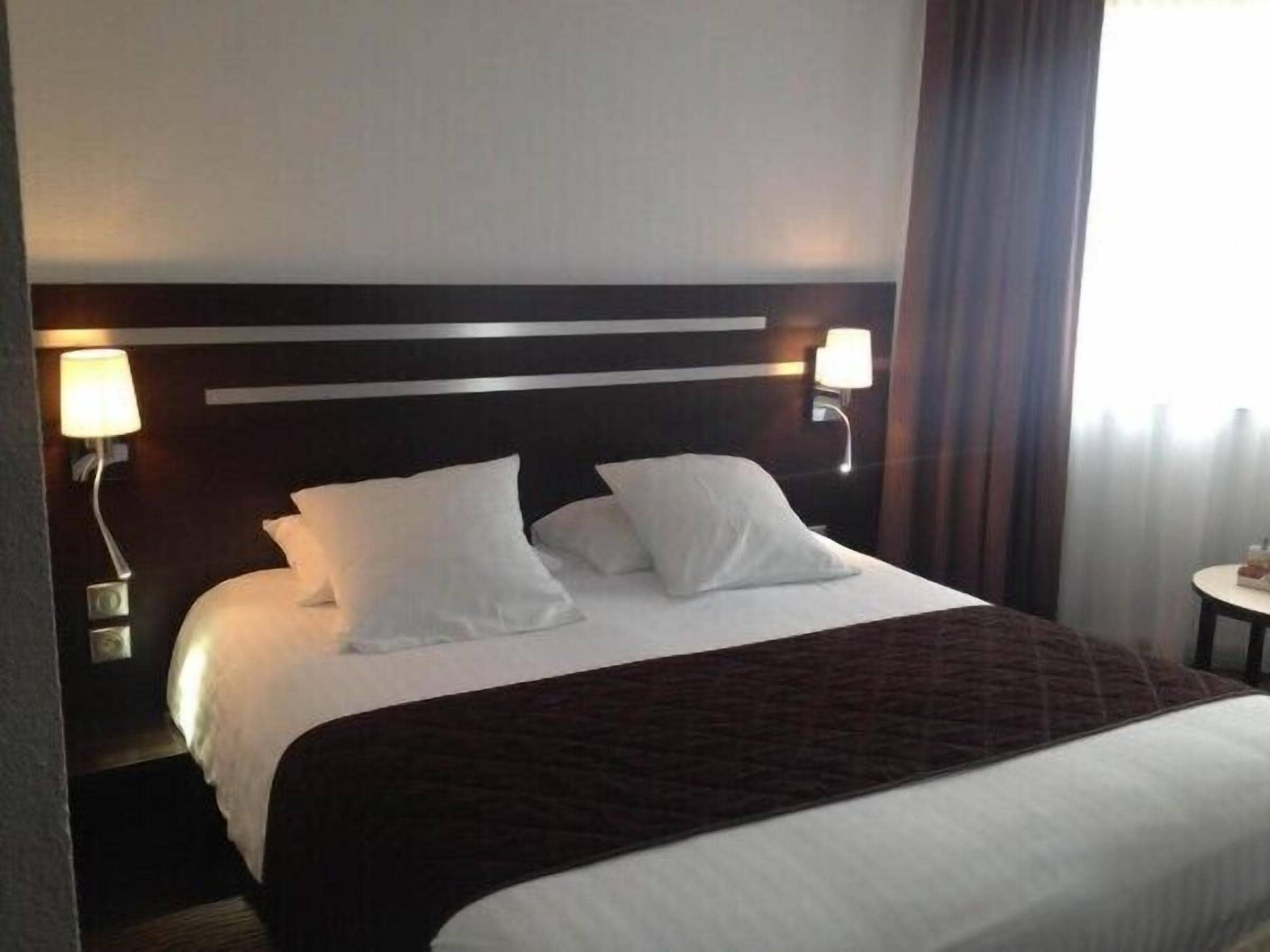 Ein Hotelzimmer mit einem großen Bett, zwei Nachttischlampen und Blick ins Freie.
