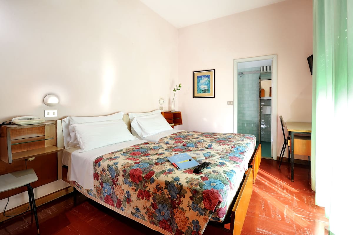 A bedroom with a bed, bedside table, lamp, and a desk with a chair.