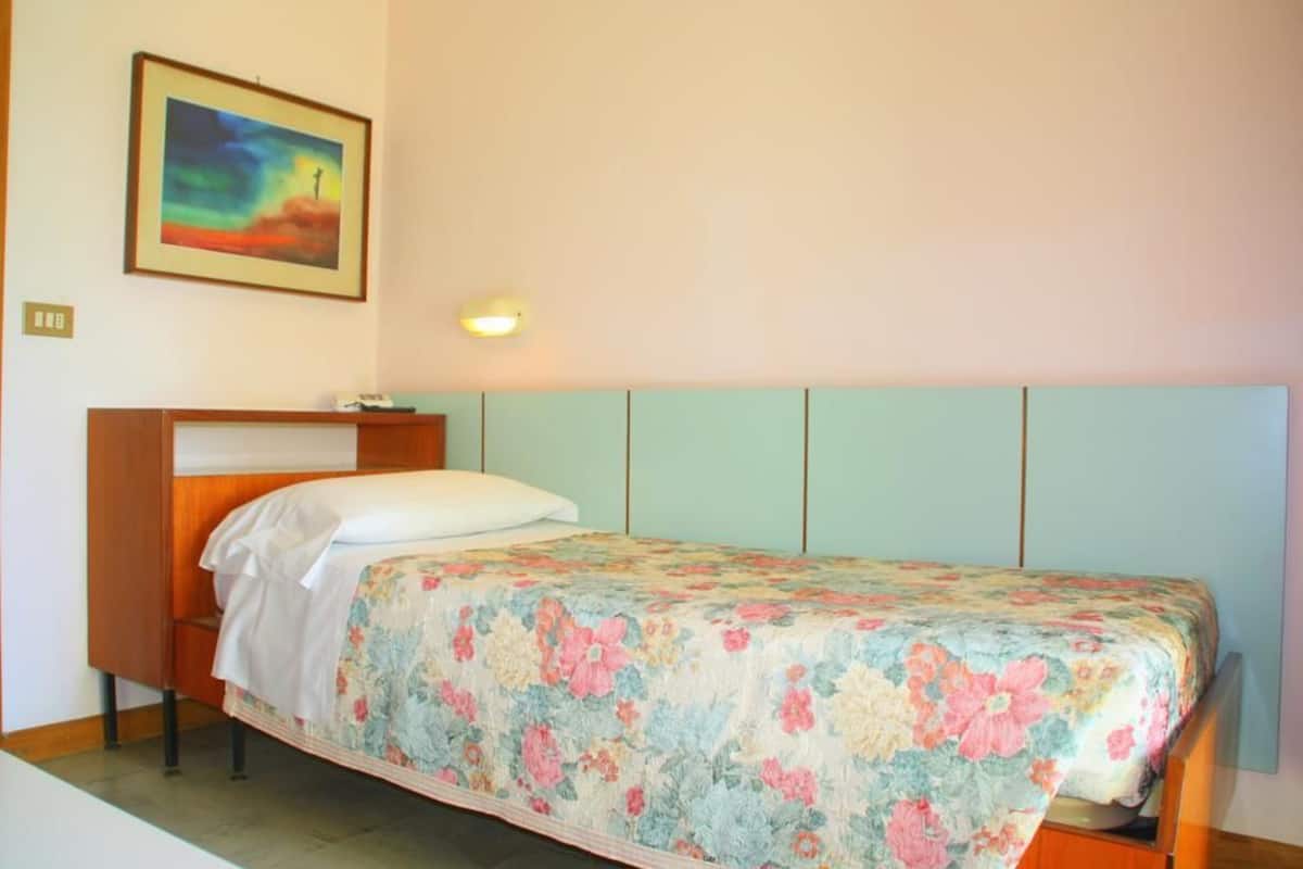 A single bed with a floral bedspread in a room with a light blue headboard and a painting on the wall.