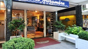 Hotel Miramare con entrada de vidrio, plantas de interior y alfombra roja.