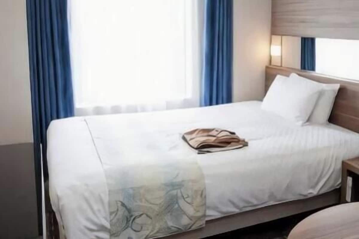 A hotel room with a bed, a nightstand, a lamp, and a window with curtains.