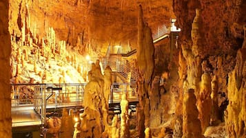 Caverna com estalactites e estalagmites, grades de metal e uma escadaria.