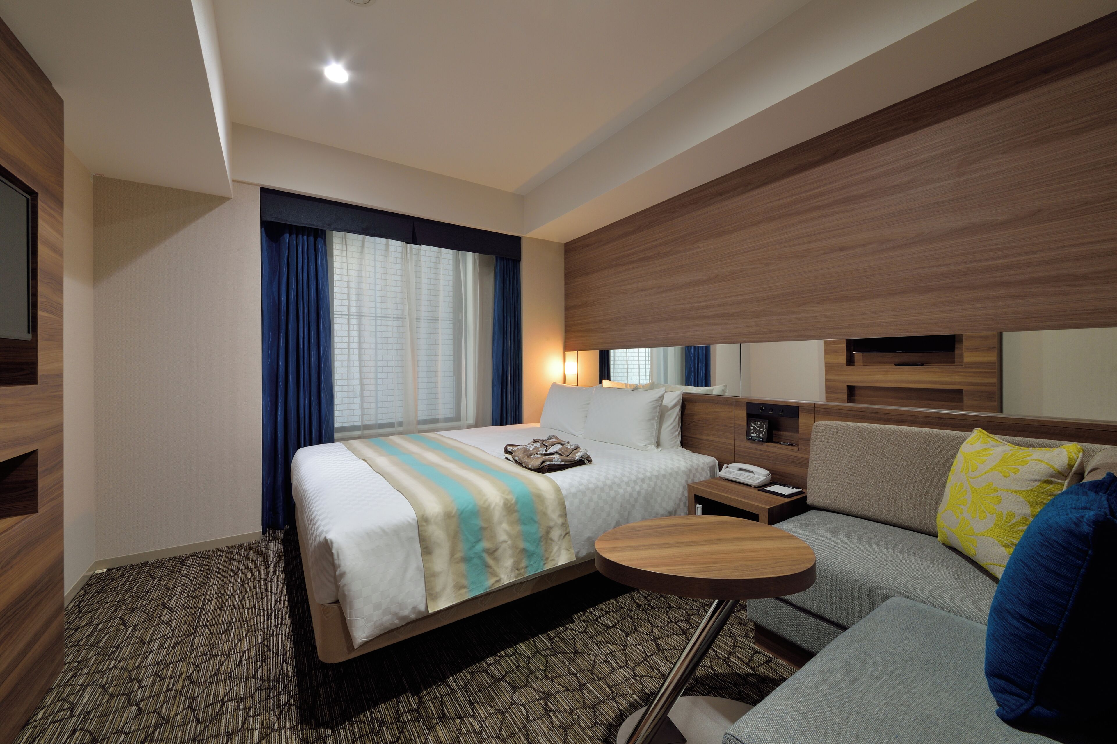 Ein Hotelzimmer mit einem Bett, einer Couch, einem kleinen Tisch, einem Nachttisch und einem Fernseher.