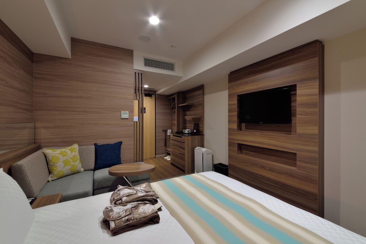 Une chambre d’hôtel moderne, équipée d’un lit, d’un canapé, d’une petite table et d’un téléviseur fixé au mur.