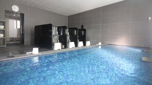 Una piscina con piso de baldosas, un reloj en la pared y una puerta a la izquierda.