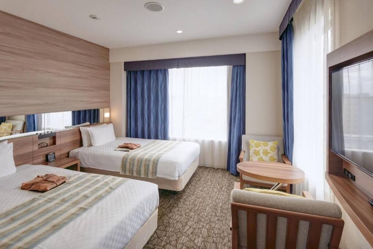 Une chambre d’hôtel avec deux lits, une petite table, un téléviseur et une fenêtre avec des rideaux.