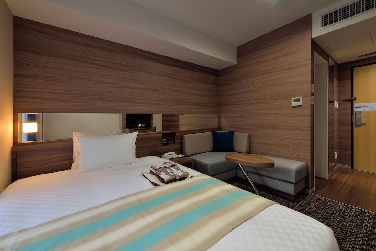 Une chambre d’hôtel moderne avec un grand lit, un petit canapé, un bureau et un miroir.