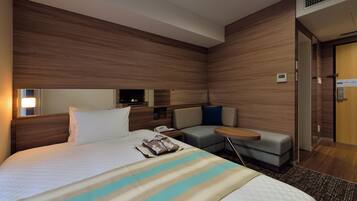 Quarto de hotel moderno com uma cama grande, um sofá pequeno, uma mesa de trabalho e um espelho.