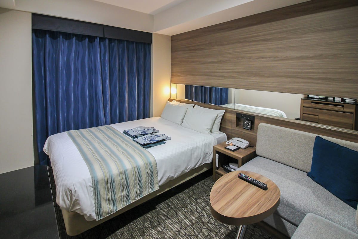 Une chambre d’hôtel comprenant un lit, un canapé, une table ronde en bois, une table de chevet avec un téléphone et un miroir.