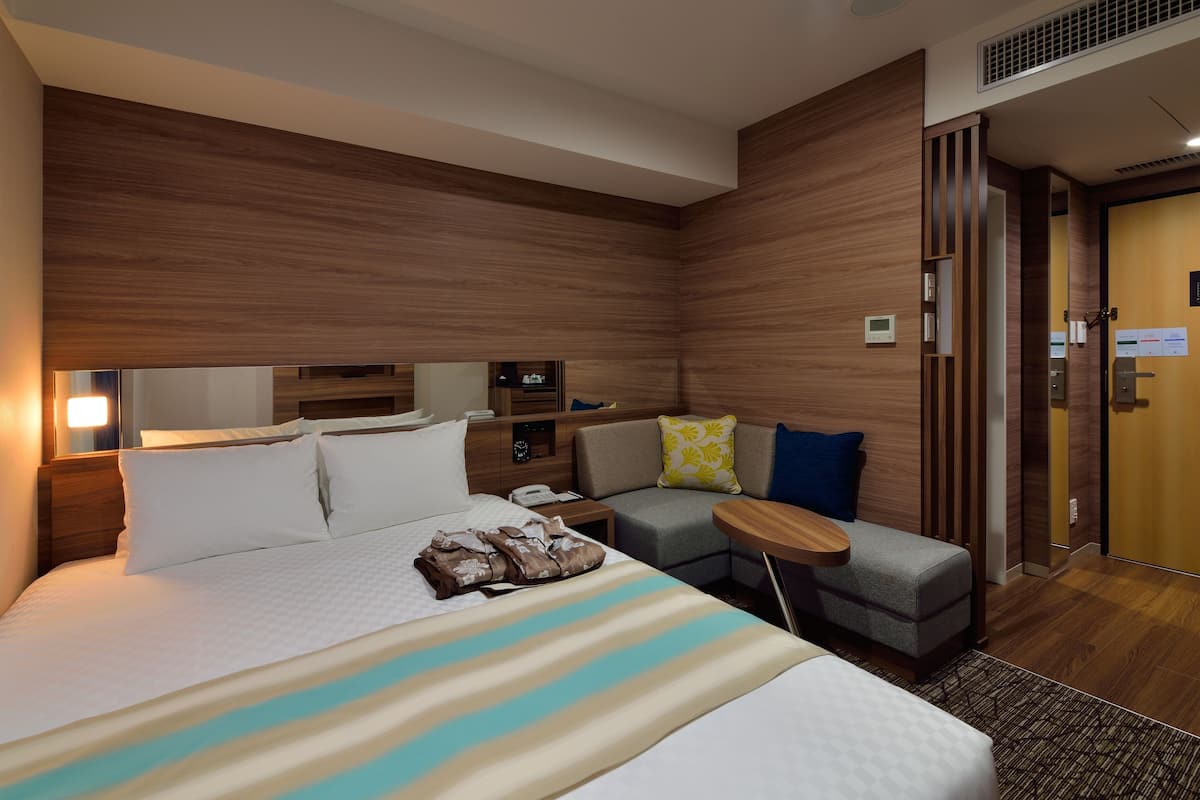 Une chambre d’hôtel avec un lit, un petit canapé, une table de chevet et un panneau mural en bois.