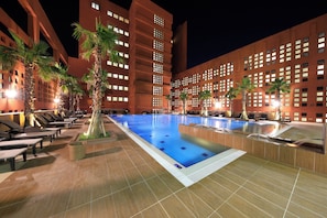 A swimming pool with lounge chairs and palm trees, surrounded by a building with multiple windows. - Booyoung Hotel & Resort (Seogwipo)