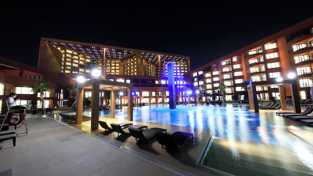 Un patio de hotel con piscina, sillones de descanso y un edificio moderno con ventanas iluminadas.