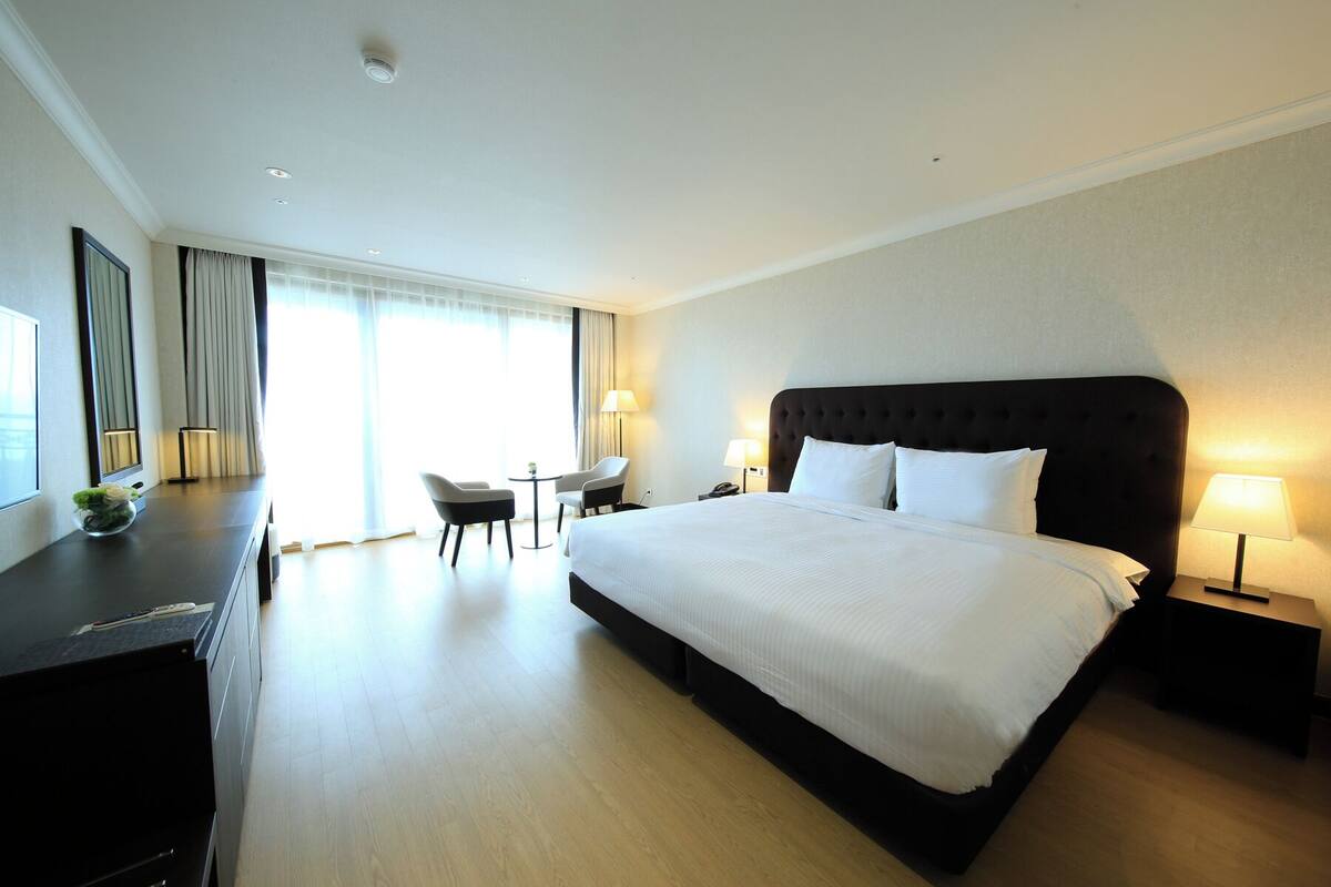 A hotel room with a large bed, a desk, two chairs, a small table, and a lamp.