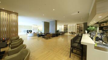A spacious lobby with a wooden floor, seating areas, and a reception desk.