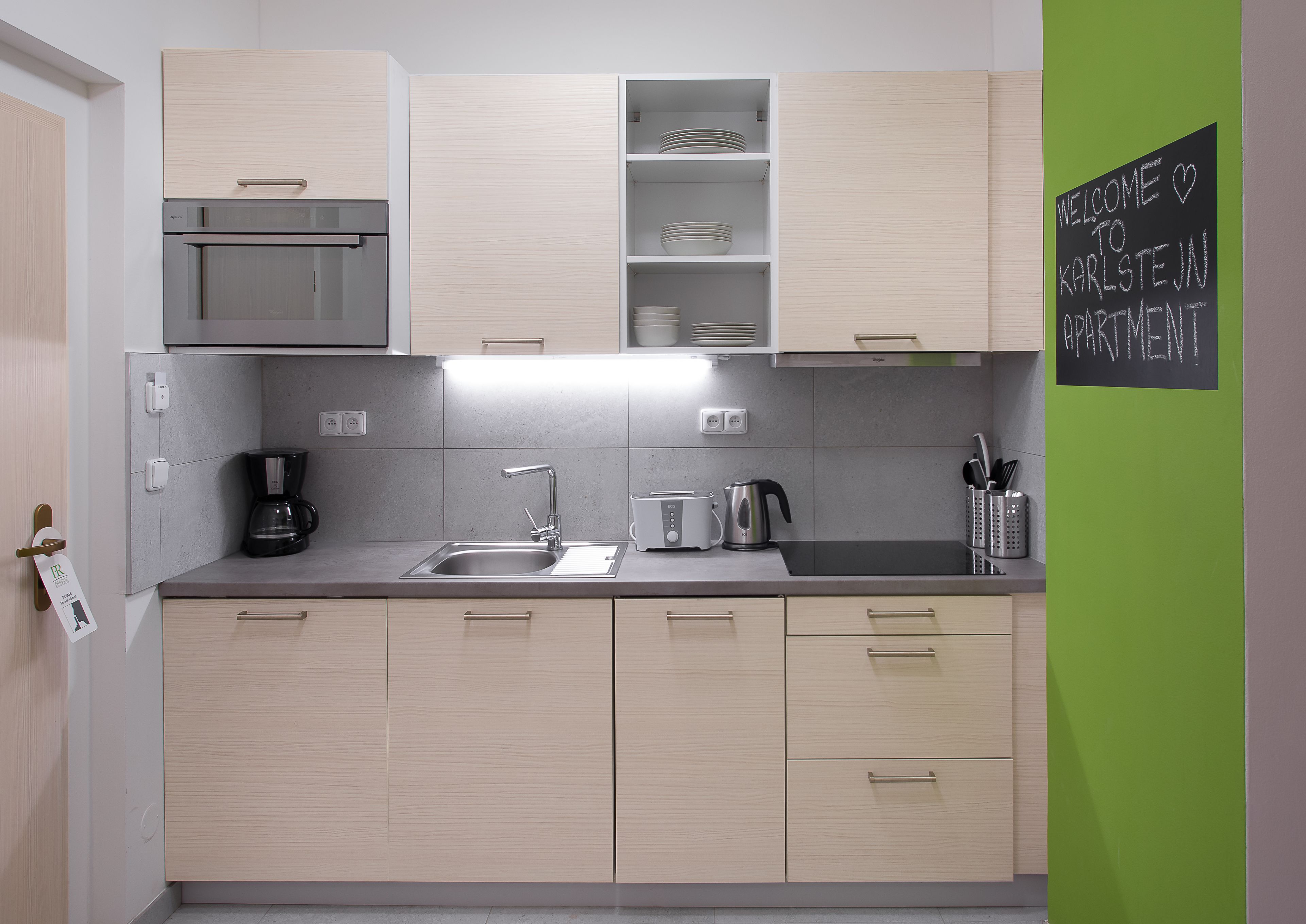 Una cucina moderna con forno integrato, macchina del caffè, tostapane e bollitore. C'è una lavagna con un messaggio di benvenuto.