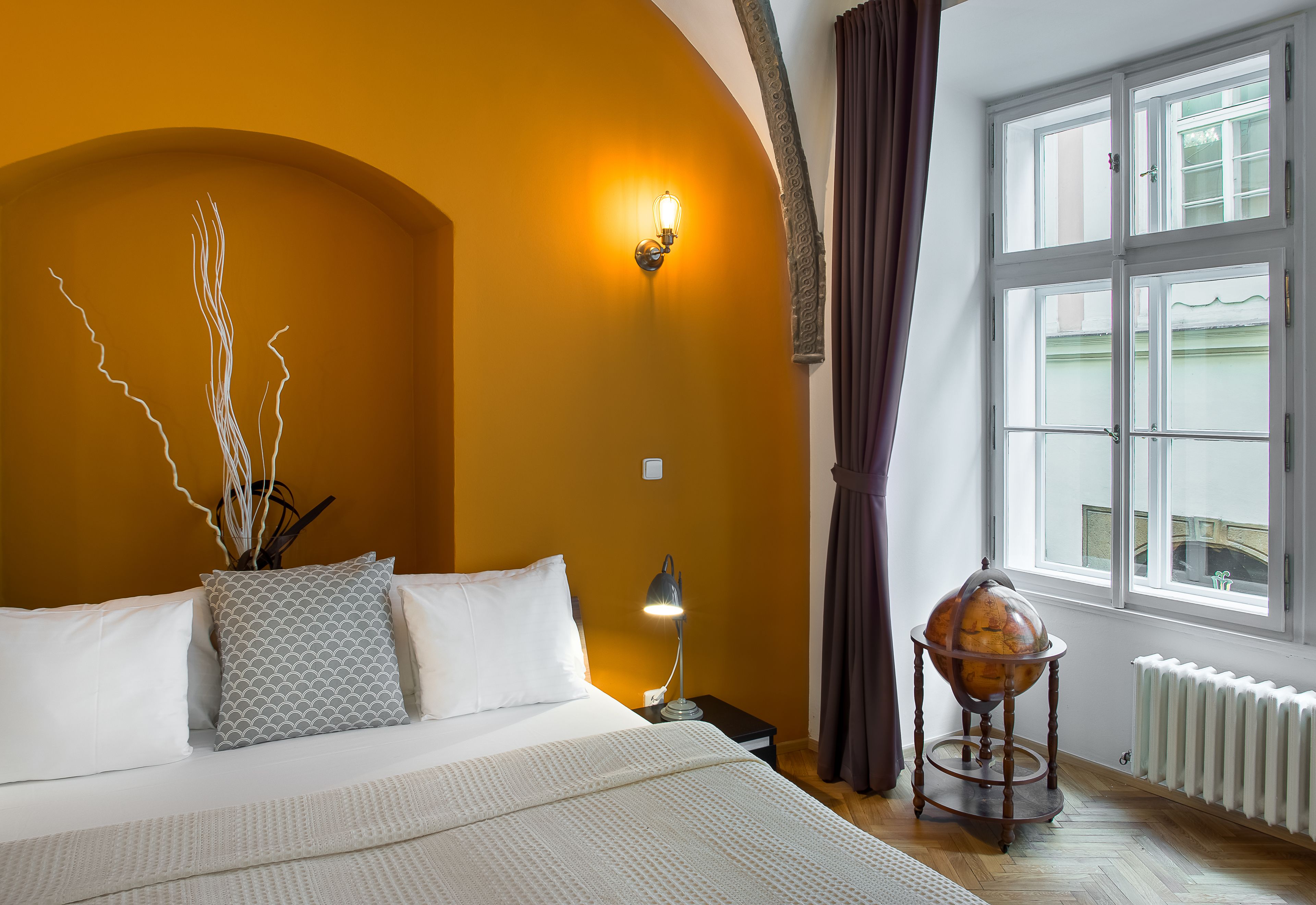 A hotel room with a bed, a globe on a side table, a lamp, and a window with curtains.