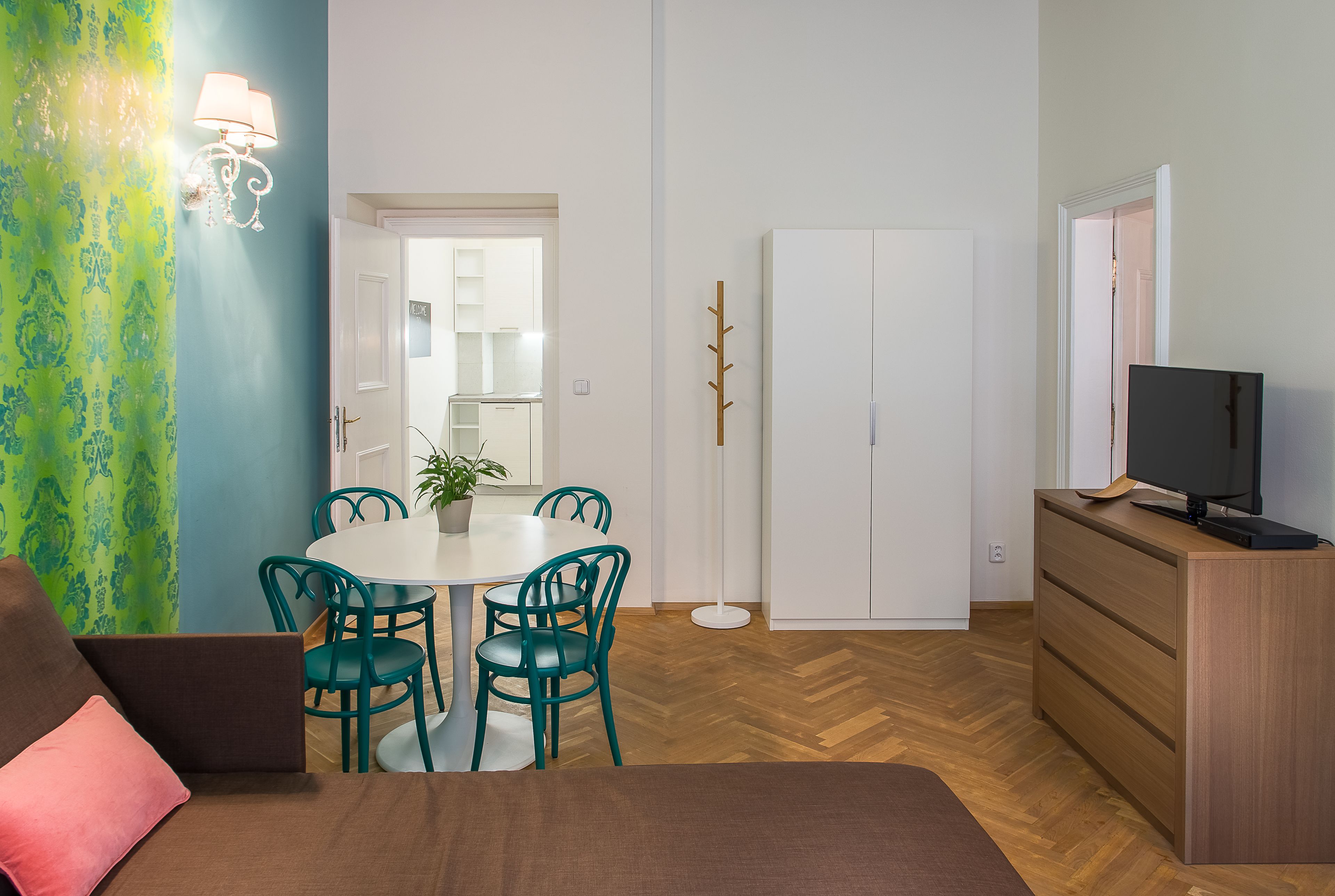 A hotel room with a bed, a desk with a TV, a dining table with chairs, and a wardrobe.