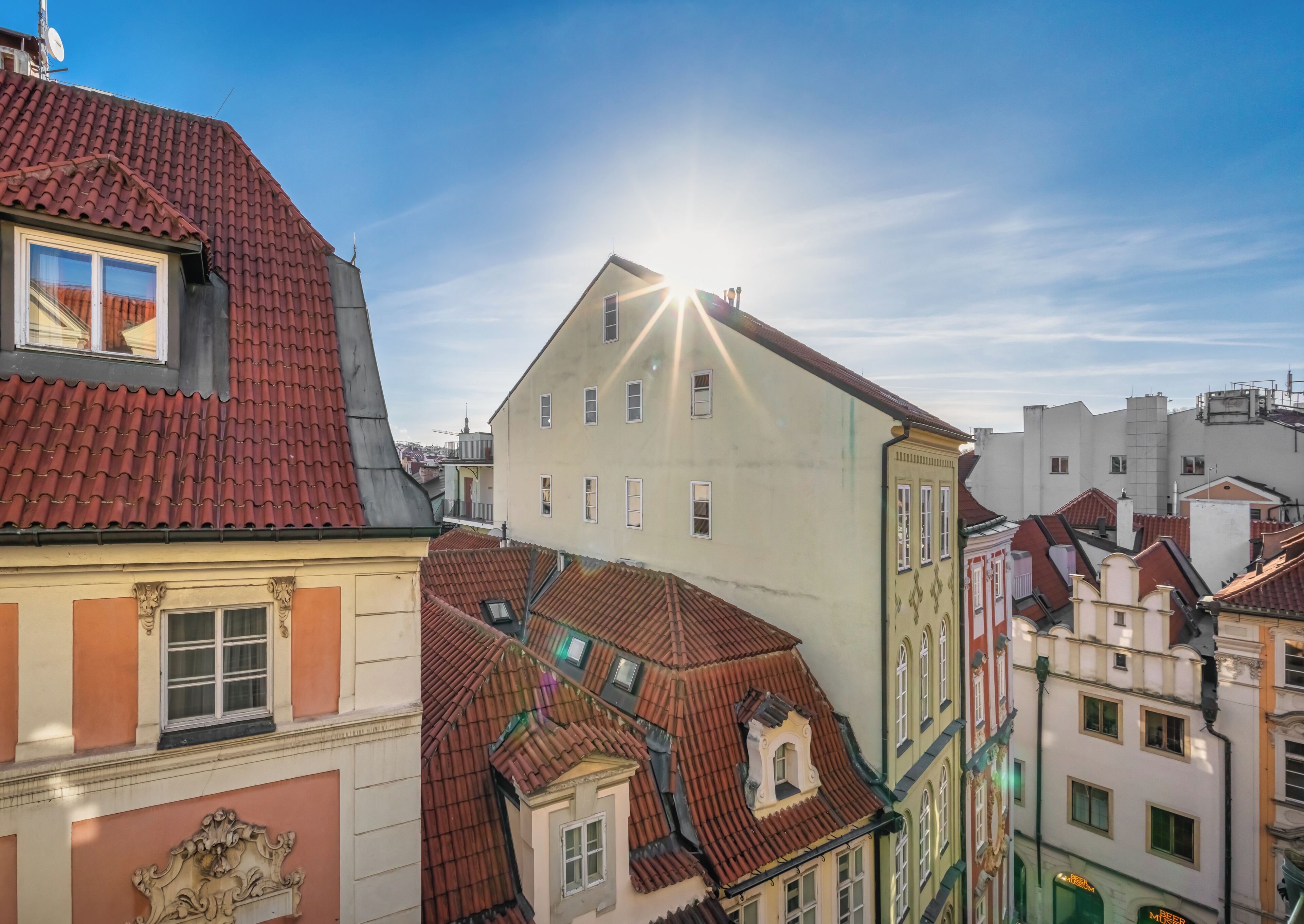 Stadtansicht mit Gebäuden und roten Ziegeldächern unter blauem Himmel.