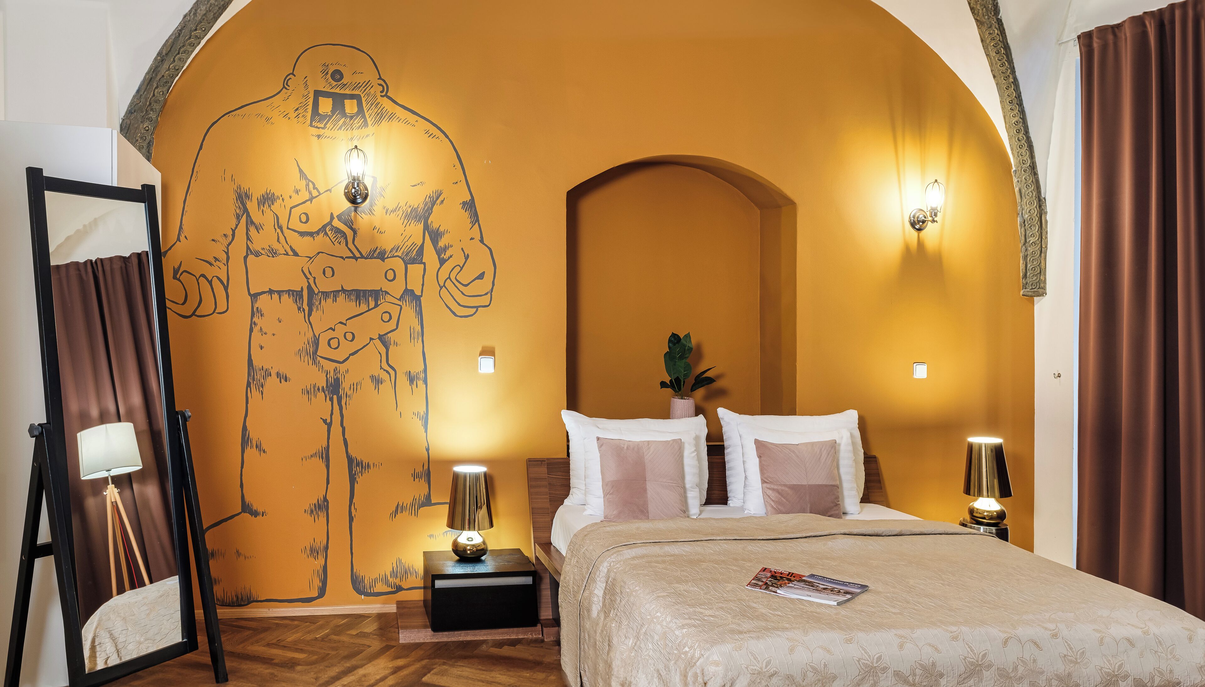 Un dormitorio con un mural grande, una cama con muchos cojines, mesitas de noche con lámparas y un espejo.