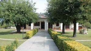 A pathway leading to a building with a solar panel on the roof, surrounded by well-maintained hedges and trees. - Relais La Mimosa (Sabaudia)